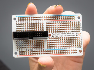 White hand holding up an assembled Adafruit Half-size Perma-Proto Raspberry Pi Breadboard PCB. A box header is soldered onto the breadboard.