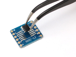 A pair of tweezers holding a microchip hovers over the SMT Breakout PCB for SOIC-12 or TSSOP-12. 