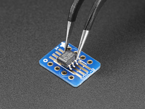 A pair of tweezers holding a microchip hovers over the SMT Breakout PCB for SOIC-8, MSOP-8 or TSSOP-8.