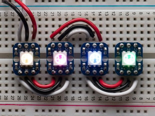 Four glowing Breadboard-friendly RGB Smart NeoPixels wired up on a breadboard