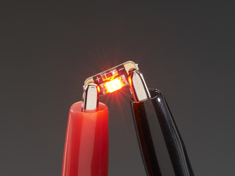 Single LED sequin PCB attached to two alligator clips, glowing red