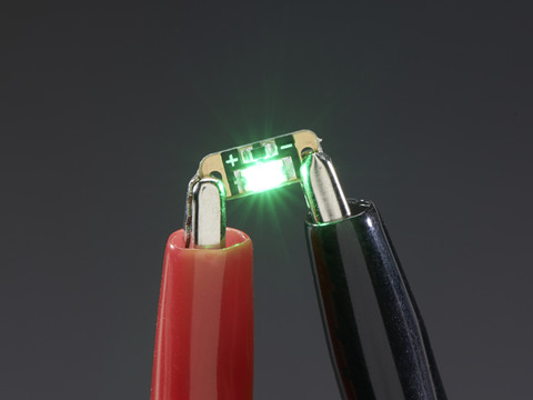 Single LED sequin PCB attached to two alligator clips, glowing green