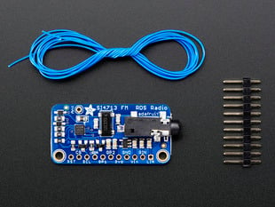 Top down view of a Adafruit Stereo FM Transmitter with RDS/RBDS Breakout next to a 11-pin header and under blue string coiled up.