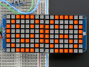 Close-up of Soldered and assembled 16x8 1.2" LED Matrix + Backpack - Ultra Bright Square Amber LEDs on a breadboard. The LED Matrices display a smiling emoji and a frowning emoji.