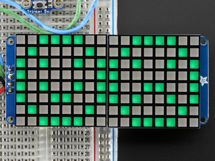 Close-up of Soldered and assembled 16x8 1.2" LED Matrix + Backpack - Ultra Bright Square Green LEDs on a breadboard. The LED Matrices display a smiling emoji and a frowning emoji.