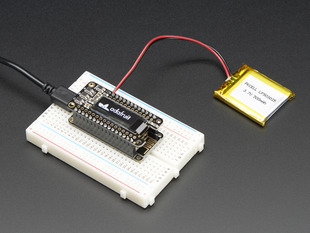 Angled shot of a Adafruit FeatherWing OLED - 128x32 OLED Add-on For Feather connected to a white breadboard and a lithium battery. 