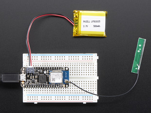 Top view of rectangular microcontroller on a white breadboard connected to a battery and an antenna. 