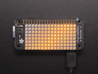 Top down view of a Adafruit CharliePlex LED Matrix Bonnet illuminating yellow. 