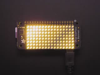 Top down view of a Adafruit CharliePlex LED Matrix Bonnet illuminating warm white. 