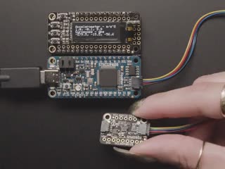 Video of a white hand moving a sensor around that connected to an OLED and a blue rectangular board. 