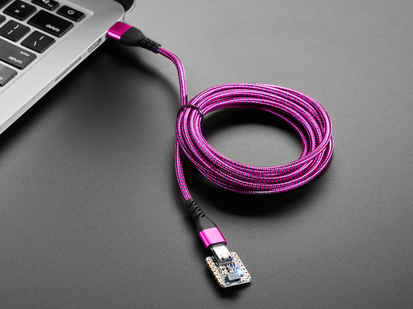 Angled shot of a pink/purple woven USB cable plugged into a laptop port and a small dev board.