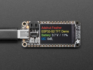 Adafruit ESP32-S2 TFT Feather powered on by a USB- C power source displaying the product tittle in a red, yellow, green, white and blue. 