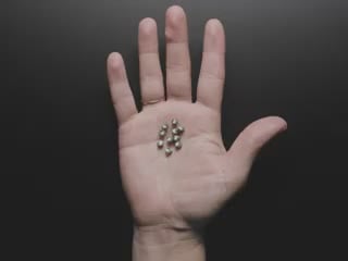 Video of a white hand holding ten wireless LED inductors in the palm of their hand. A small inductive coil is placed over the LEDs which light up red.