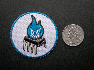 Circular embroidered badge with an evil blue flame over an OpAmp on white background with blue trim. Shown next to a quarter for scale. 