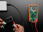 Overhead lifestyle image of cable and adapter hooked up to a multimeter displaying 19.9V.