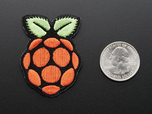 Embroidered patch in the shape of the raspberry pi logo, in red with green leaves on top, outlined in black. Shown next to quarter for scale. 